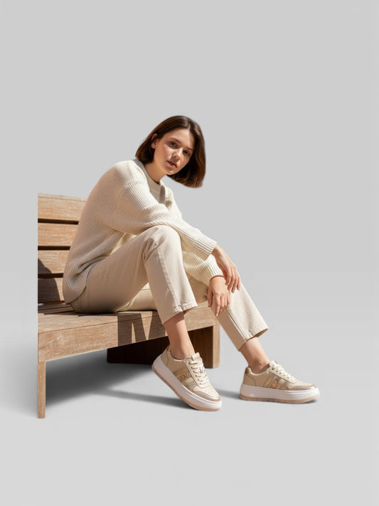 Mujer sentada en banco usando tenis gavani shoes co de cuero champaña con suela cómoda y diseño casual moderno.